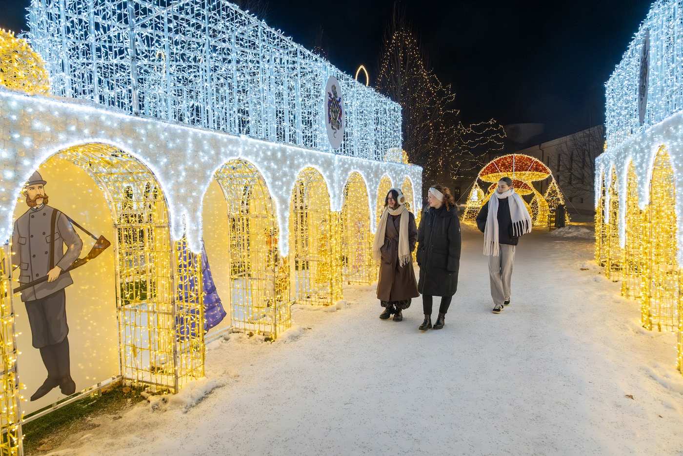Visitors walking through an illuminated white arcade with a figure sculpture at the side
