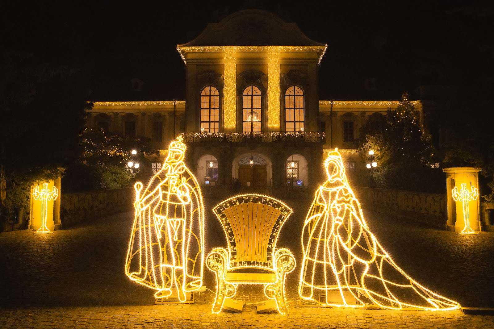 Light silhouettes of a king and queen with a throne in front of a lit palace